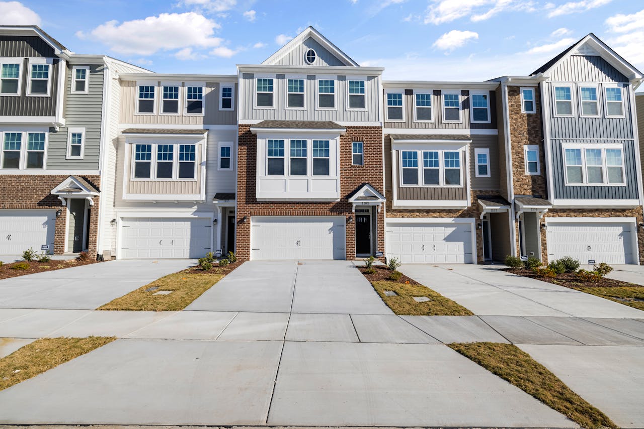gallery-6 Row of modern townhouses with spacious driveways and garage fronts under blue sky.