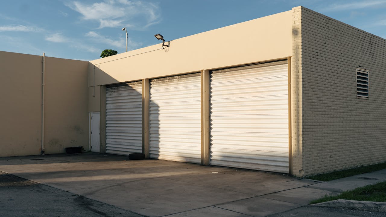 our-services-1 Exterior view of a beige industrial building with three closed garage doors under a clear sky.
