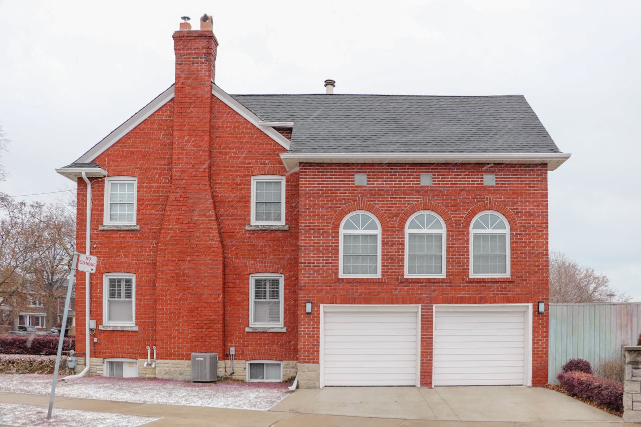 hero-img-02 Red brick house exterior in Toronto with arched windows, chimney, and double garage.